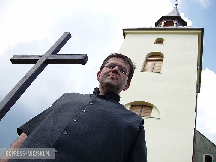 Proboszcz Zbigniew Słobodecki na tle kościoła w Księginicach Małych. Na wieży nowa kula ze stali kwasoodpornej